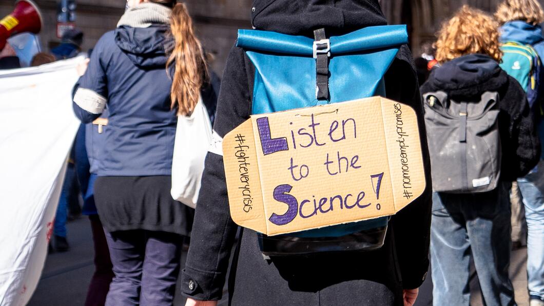 Beeld van een protestbord met daarop 'Listen to the science!'