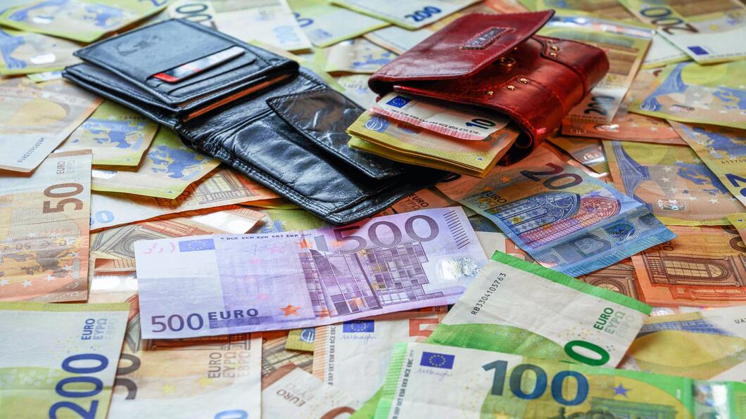 een tafel vol met eurobiljetten variërend van 20 tot 500 euro. Daar bovenop liggen twee portemonnees waar geldbiljetten uitpuilen.