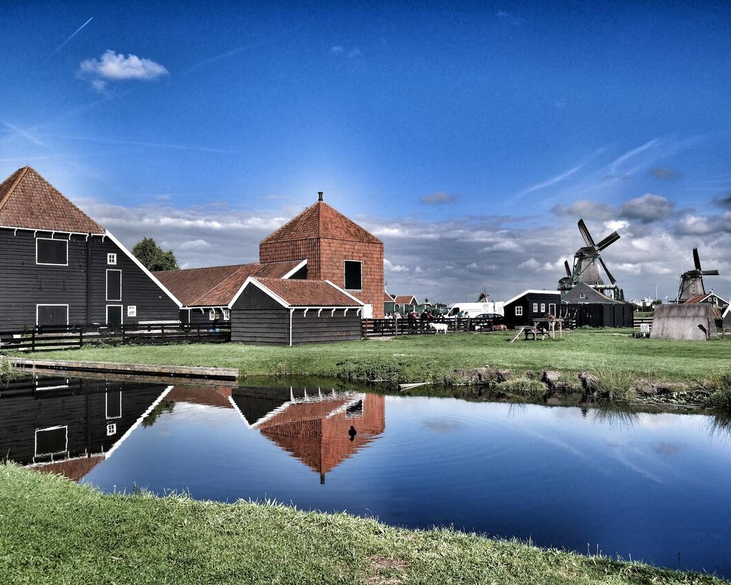 Nederlands landschap waarop een riviertje te zien is wat door een weiland loopt, met daarop molens en boerderijen. 